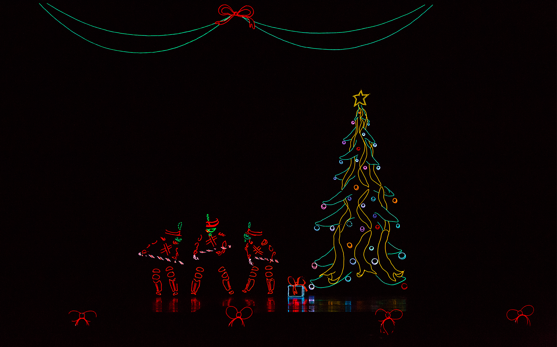 dark stage with people in black costumes with lights on them and a lighted christmas tree