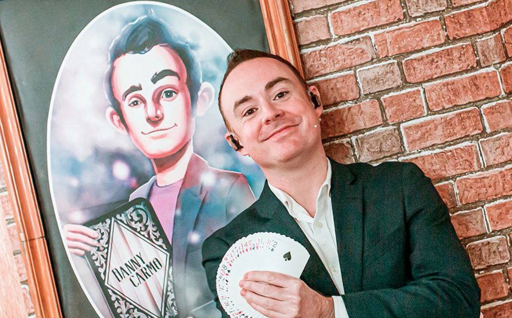 Danny holding a spread of cards in front of cartoon image of himself