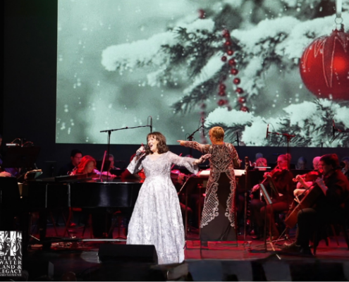 Colleen Raye A Holiday in Your Heart - Dec 8 woman singing on stage in front of a christmas scene and an orchestra