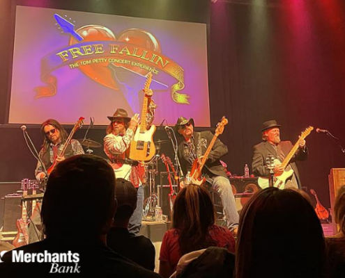 Free Fallin' The Tom Petty Experience - Apr 3 band on stage holding guitars in front of sign that says free fallin