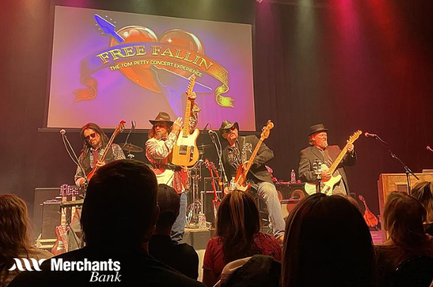 Free Fallin' The Tom Petty Experience - Apr 3 band on stage holding guitars in front of sign that says free fallin