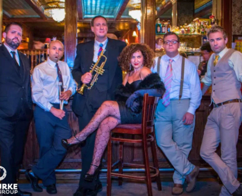 Swing Makes You Sing - Apr 8 woman in a chair in front of a bar surrounded by male band mates