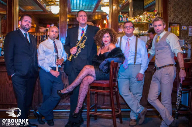 Swing Makes You Sing - Apr 8 woman in a chair in front of a bar surrounded by male band mates